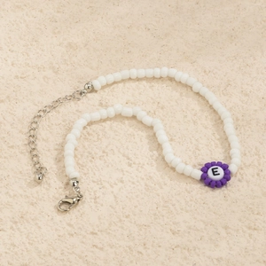 Detalle de pulsera de cuentas blancas con flor púrpura y colgante de letra E