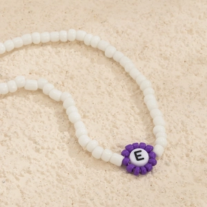 Vista macro de collar de cuentas blancas con colgante de flor púrpura y cuenta de letra E