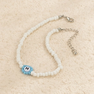 Detalle de collar de cuentas con flor azul claro, colgante de letra H y cierre de mosquetón