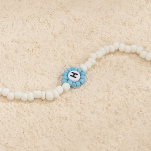 Detalle de collar de cuentas hecho a mano con flor azul y cuenta acrílica con letra H