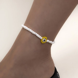Detalle de collar de cuentas con flor amarilla y la letra W en cuentas blancas