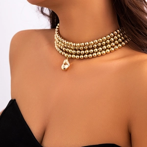 Close-up of triple-layered gold beaded necklace with a polished teardrop pendant
