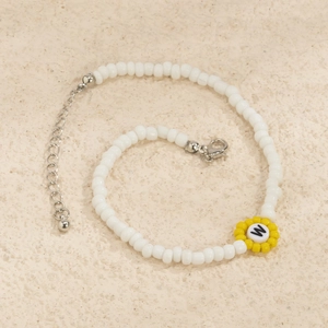 Primer plano de pulsera de cuentas blancas con girasol amarillo y letra W grabada