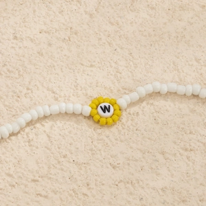 Primer plano de collar artesanal con cuentas blancas y dije de girasol con la letra W grabada