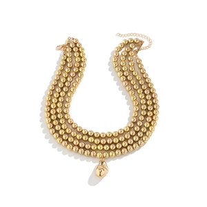 Macro detail of triple-layer gold beaded necklace with metallic bean pendant and lobster clasp