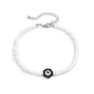 Detalle de collar de cuentas blancas con flor negra y colgante de la letra N