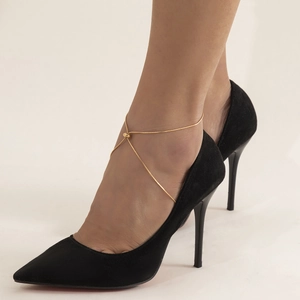 Detail of adjustable gold beaded anklet worn with black pointed-toe stiletto heels