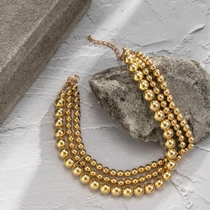 Macro detail of triple-layered gold bead necklace with lobster clasp on natural stones