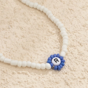 Detalle de pulsera de cuentas blancas con flor azul y cuenta con la letra R en negro