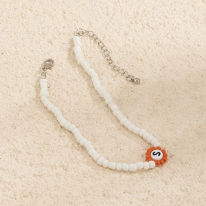 Detalle de collar de cuentas de colores con amuleto de flor naranja y colgante letra S