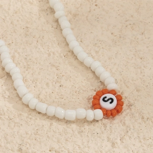 Primer plano de un collar de cuentas con un elemento floral y un colgante de letra S
