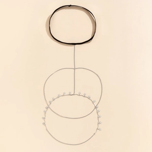 Detail of silver thigh chain featuring geometric stars and black elastic straps on beige