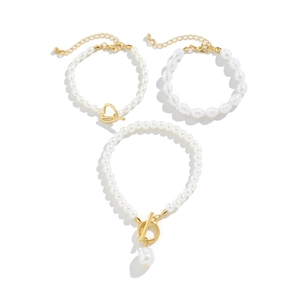 Detailed view of three layered pearl bracelets with gold heart-shaped OT toggles and charms