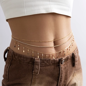 Détail d'une chaîne de taille dorée multicouche avec strass et pendentifs métalliques