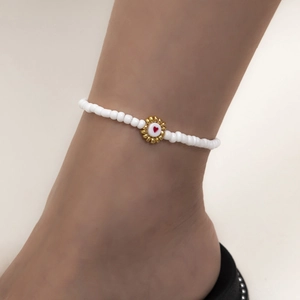 Detalle de tobillera de cuentas blancas con colgante de corazón dorado en tobillo