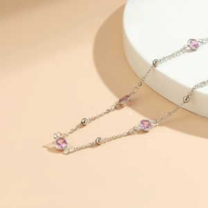 Detail of silver chain with pink gemstones and beads on a minimalist stone display