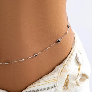 Detail of silver body chain featuring black geometric charms and metallic beads on model