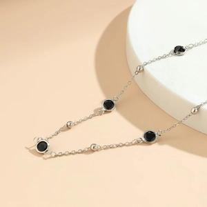 Macro detail of silver body chain featuring black gemstones and polished round beads