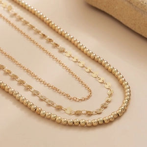 Détail d'une chaîne perlée dorée multicouche avec paillettes et textures métalliques