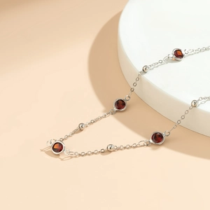 Macro detail of silver bead chain body jewelry featuring round red gemstones in bezel setting