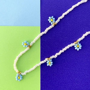Dettaglio della collana di perline fatta a mano con margherite blu su sfondo di carta vivace