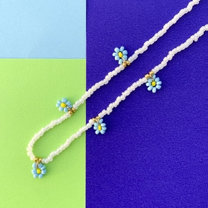 Dettaglio di ciondoli margherita blu e perline bianche su una collana di perline colorate