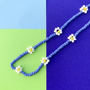 Macro di collana con perline blu e ciondoli a forma di margherita bianchi e gialli fatti a mano