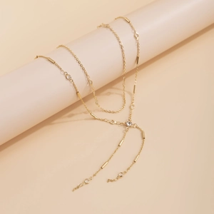Detail of layered gold body chain featuring crystal accents and metal beads on a pedestal