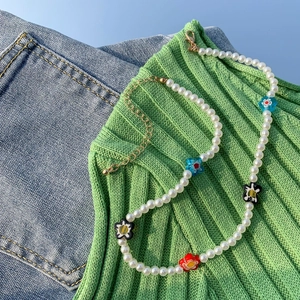 Dettaglio della collana di perle finte e fiori in resina colorati su sfondo verde