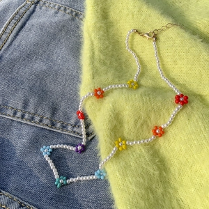 Dettaglio della collana di perle con margherite intrecciate colorate e chiusura dorata