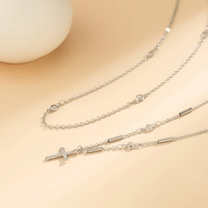 Detail of silver layered necklace with crystal cross pendant and metallic cylinder accents