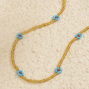 Detail of handmade gold seed bead body chain featuring small light blue daisy flowers
