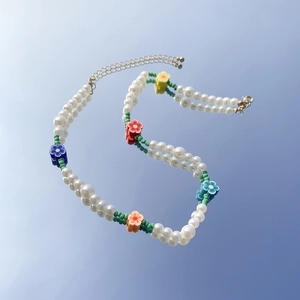 Dettaglio della collana di perle finte con margherite colorate su uno sfondo specchiato