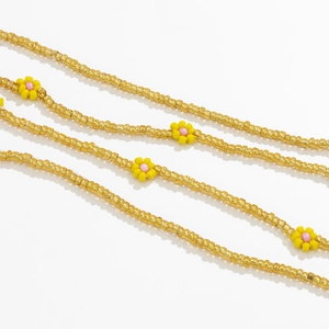 Macro detail of gold-beaded body chain featuring delicate yellow and pink flower charms