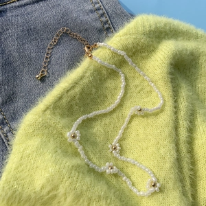Dettaglio della collana di perline a margherita bianca con chiusura dorata su denim blu