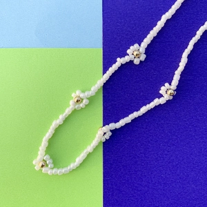 Dettaglio della collana di perline bianche con accenti dorati a forma di fiore