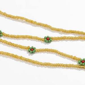Detail of yellow bead body chain with handmade green and red beaded flower patterns