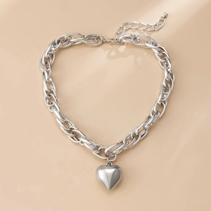 Collana a catena spessa argentata con ciondolo a cuore lucido su uno sfondo beige chiaro