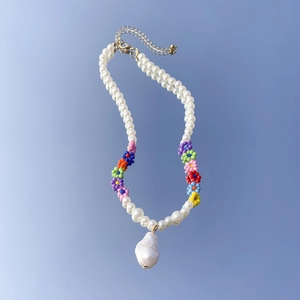 Dettaglio della collana a margherita con perla barocca su specchio con cielo blu