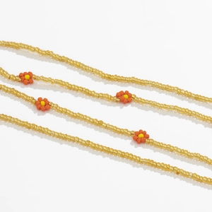Macro detail of handmade yellow and orange seed bead daisy body chain on white surface