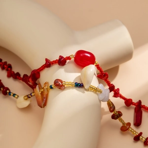 Dettaglio catena da vita boho con perline rosse, accenti dorati, conchiglie e pietre grezze