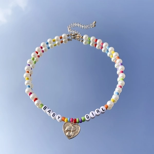 Dettaglio della collana di perle colorate con lettere BABY GIRL e ciondolo a cuore