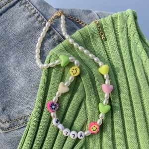 Dettaglio della collana con perle barocche, cuori colorati e scritte SALLY su denim