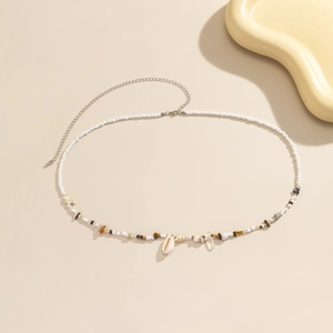 Detalle de cadena de cintura boho con cuentas blancas, piedras y un colgante de concha