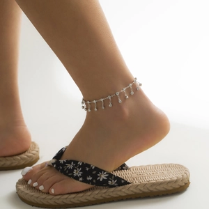 Close-up of silver anklet with rhinestone pendants on woman's foot in beach sandals