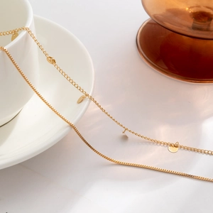 Detail einer goldene Körperkette mit Pailletten auf einer weißen Porzellantasse