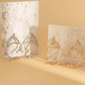 Gold and silver hollow feline elf ear cuffs displayed on natural stone pedestals