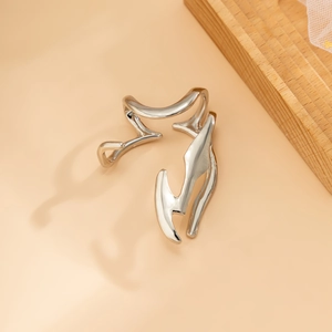 Detail of silver liquid metal ear cuff with irregular streamlined design on a beige background