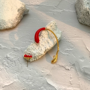 Detailed close-up of golden rhinestone ear cuff with red enamel accents on stone base