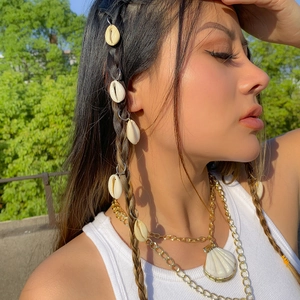 Close-up of bohemian cowrie shell hair clips and gold layered necklaces on a model